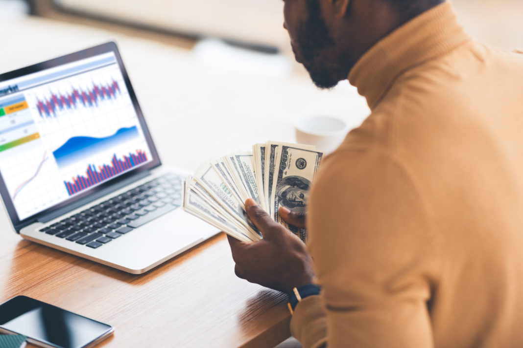 black manager working with diagrams on pc holding dollars