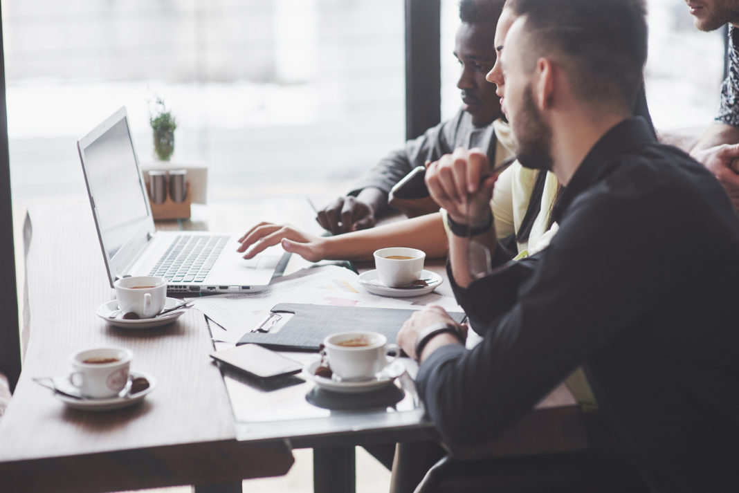 multi ethnic business people, entrepreneur, business, small business concept, woman showing coworkers something on laptop computer as they gather around a conference table